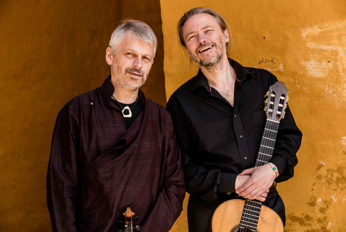 Studio portrait of a classical music trio (clarinet, piano, and cello) in black attire in front of a grand piano.