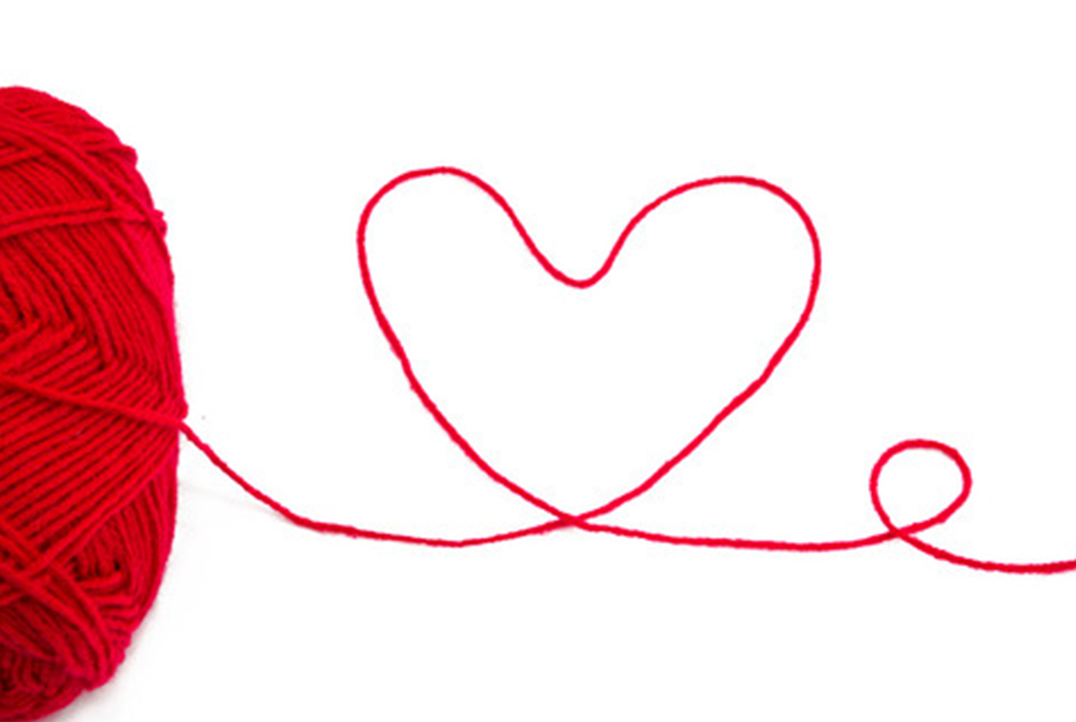 Et nærbillede af et rødt garnnøgle, hvorfra en rød tråd løber ud og danner en hjerteform mod en hvid baggrund.