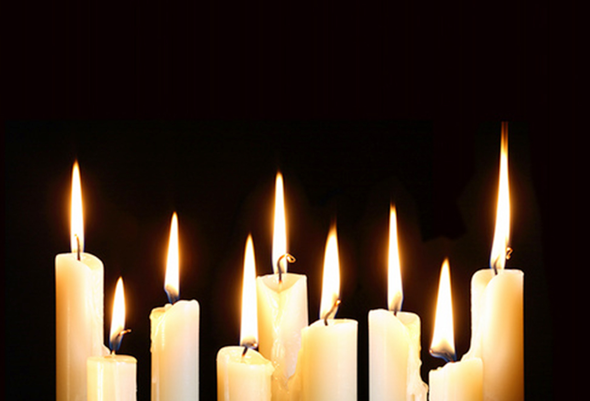 En række brændende hvide lys i forskellige højder mod en mørk, sort baggrund.
